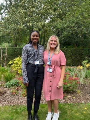 Occupational health nurses Delase Tettey and Helen Gaughan stood outside in a garden. They are smiling in the photograph.